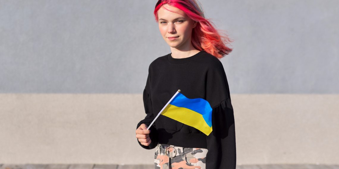 Female student teenager with Ukraine flag, gray outdoor wall background. Ukraine, education and youth, patriotism people concept. Public media Ukraine