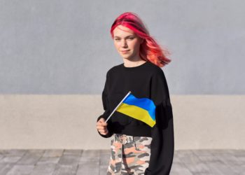 Female student teenager with Ukraine flag, gray outdoor wall background. Ukraine, education and youth, patriotism people concept. Public media Ukraine